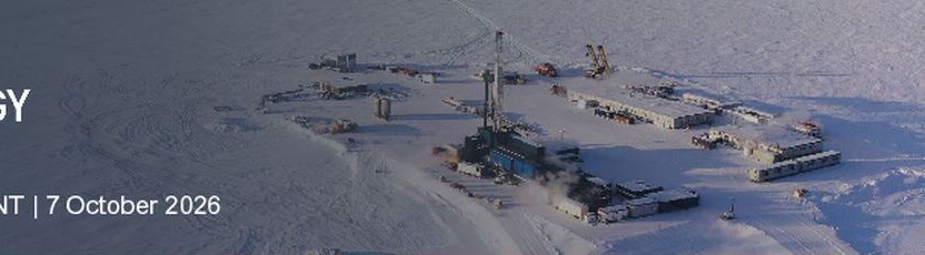 Aerial photograph of a snow-covered Arctic industrial drilling site with a derrick, equipment and vehicle tracks.