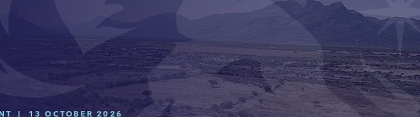 Aerial view of a low industrial complex and cleared terrain set against mountains, under a dark blue graphic overlay.