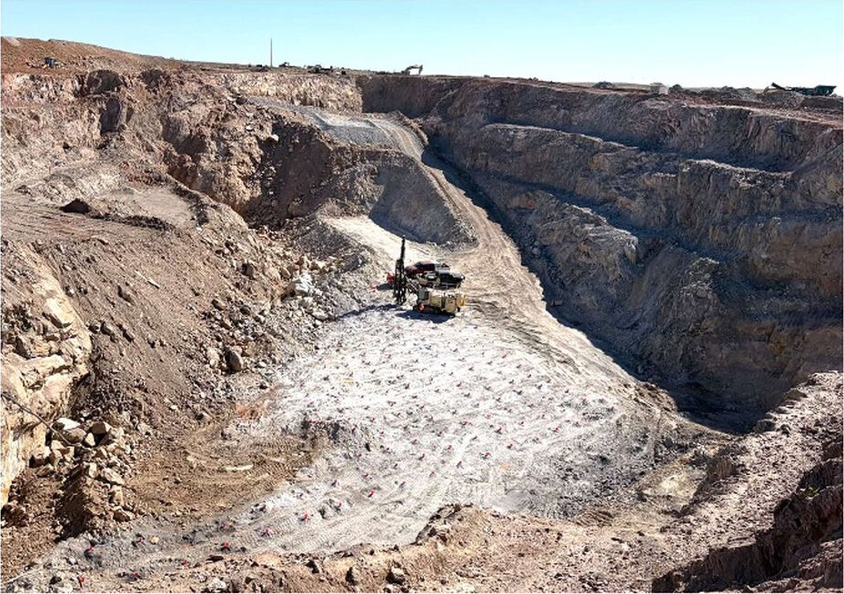 Open-pit mine with terraced rock walls, a haul road and mining equipment on the pit floor.