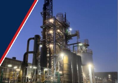Industrial processing plant towers, piping and tanks illuminated at dusk.