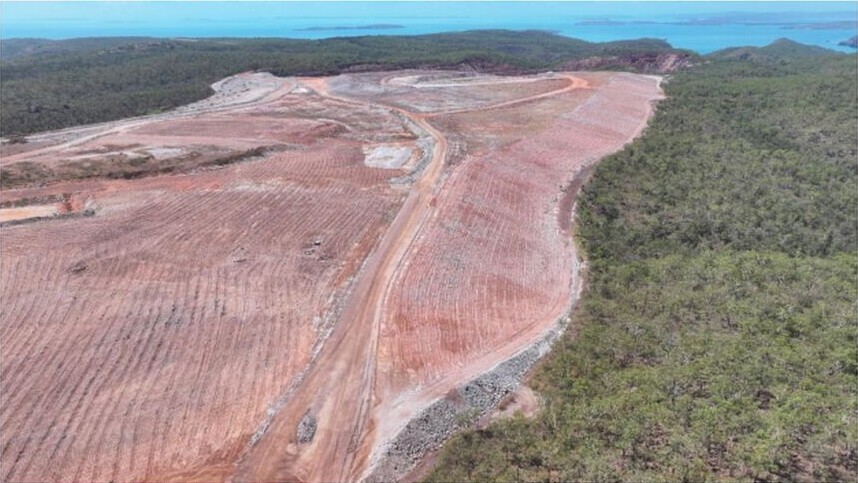 Aerial view of broad graded reddish earthworks and a rehabilitated waste-dump area surrounded by dense green vegetation on Koolan Island.