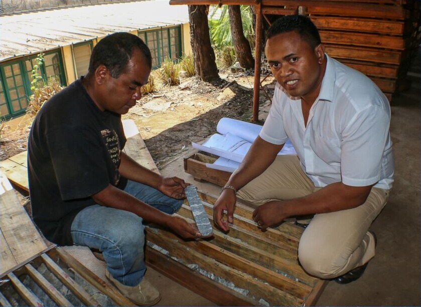 Two men examine graphite core samples laid out in wooden trays at the Maniry Graphite Project in Madagascar.