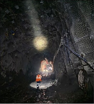 Underground exploration decline with a small orange mining vehicle beneath rock-supported tunnel walls.