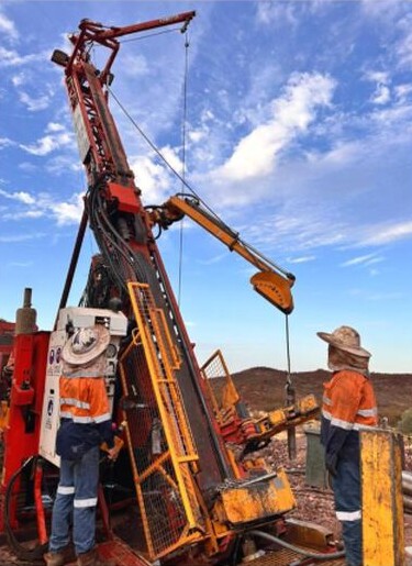 Workers beside a tall drilling rig operating in rocky terrain at the Ashburton Gold Project.