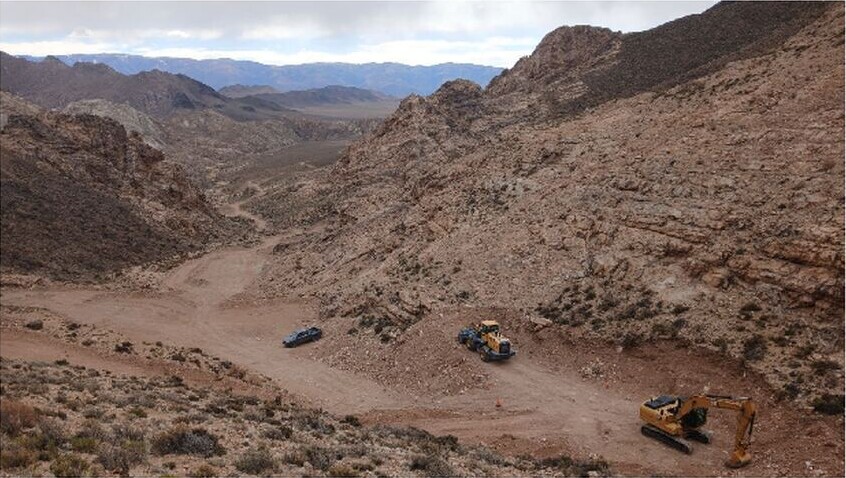 Rocky desert valley at Las Opeñas with a dirt access track, two excavators and a vehicle beneath steep brown ridges.