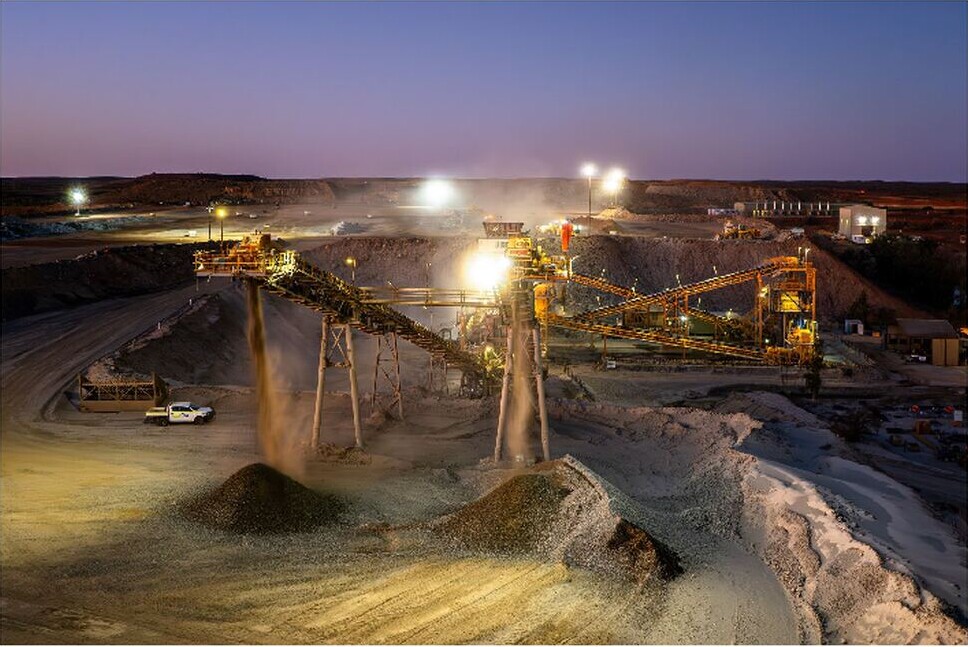 Night-time view of a gold processing plant, conveyors and ore stockpiles illuminated by work lights.