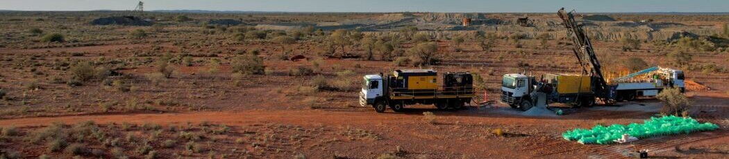 Drilling rig and support trucks operating on a red-earth exploration site at Mt Ida.