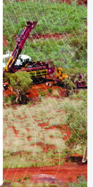 Drilling rig operating on red earth amid low scrub vegetation at the Smokebush project.
